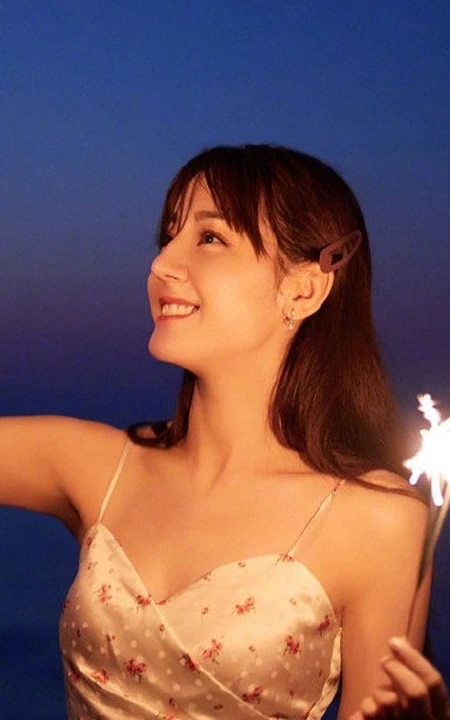 迪丽热巴着肩带裙夜晚海边唯美写真，手拿烟花笑容灿烂