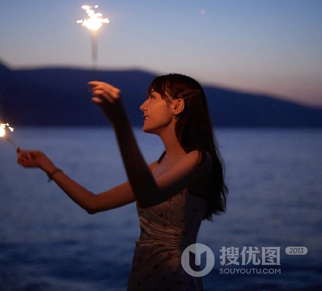 迪丽热巴着肩带裙夜晚海边唯美写真，手拿烟花笑容灿烂