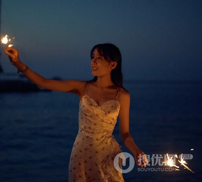 迪丽热巴着肩带裙夜晚海边唯美写真，手拿烟花笑容灿烂