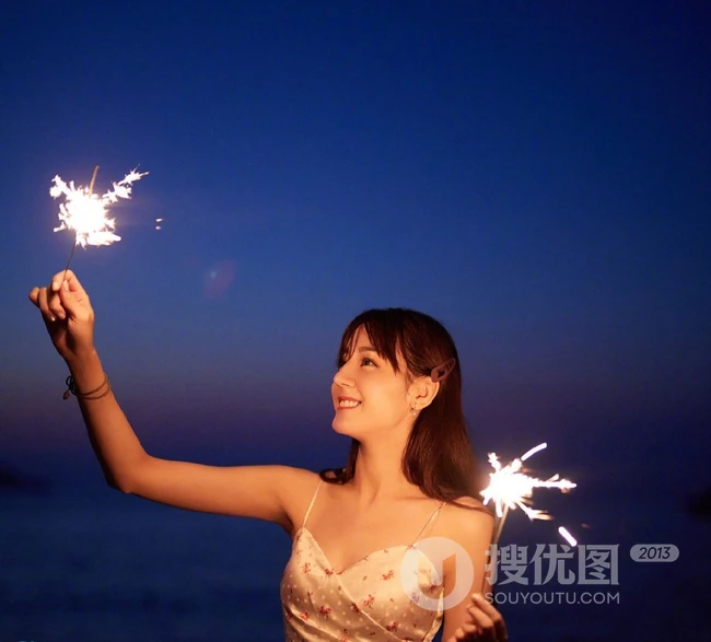 迪丽热巴着肩带裙夜晚海边唯美写真，手拿烟花笑容灿烂