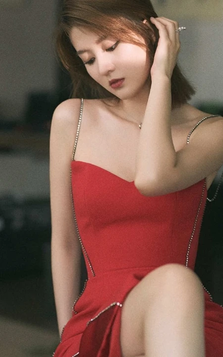 女生乔欣肩带红裙气质出镜，双腿交叉静坐姿态动人