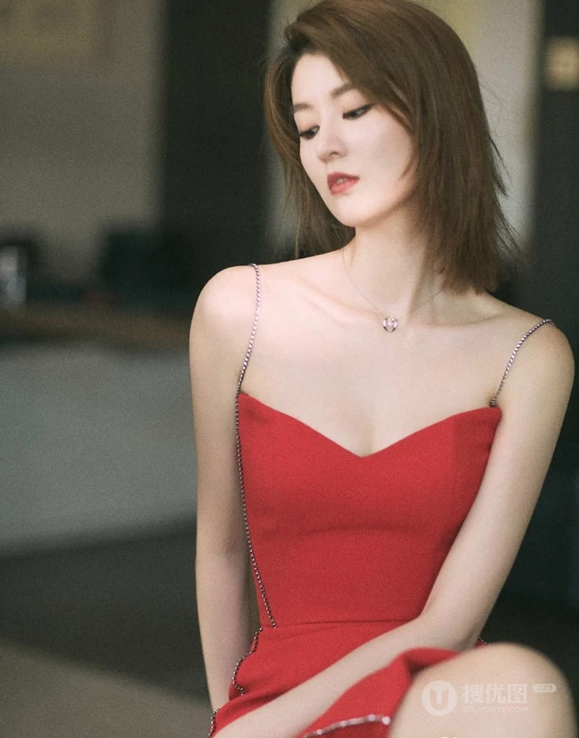 女生乔欣肩带红裙气质出镜，双腿交叉静坐姿态动人