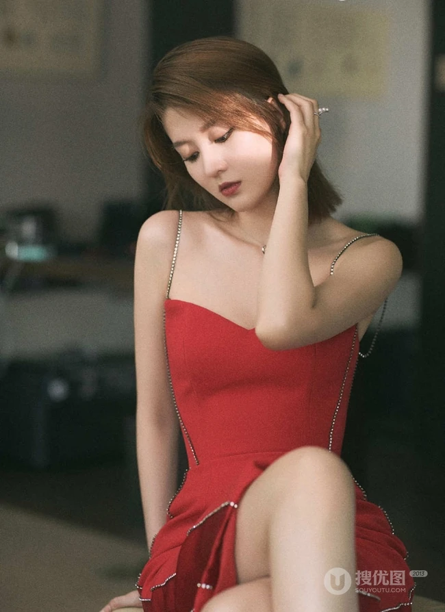 女生乔欣肩带红裙气质出镜，双腿交叉静坐姿态动人