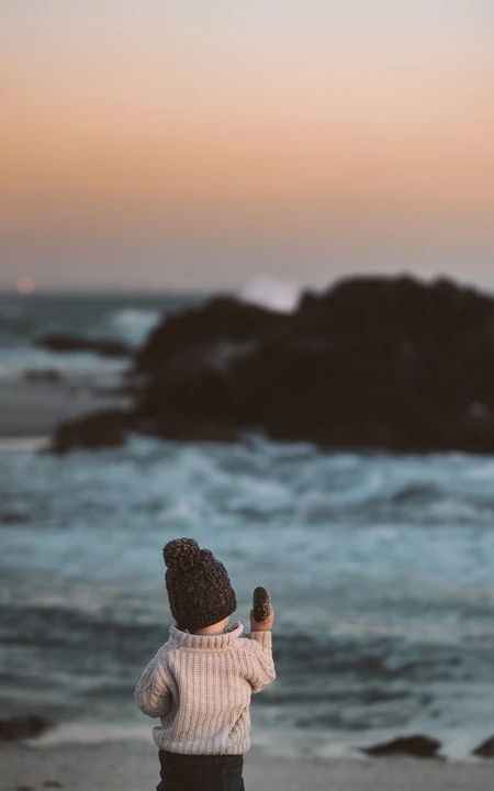 海边沙滩上的戴羊毛帽子的萌娃手机壁纸