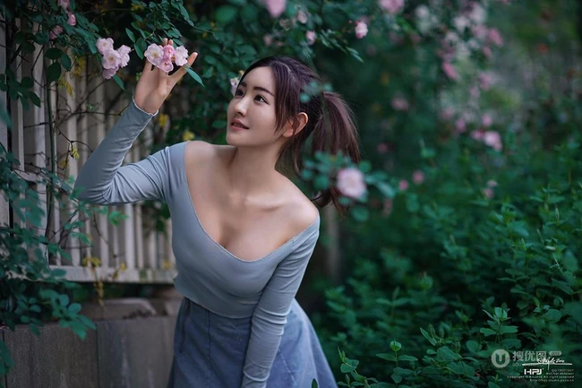 气质美丽女孩蔷薇花前驻足流连，着V领上衣搭牛仔裙艺术摄影图片