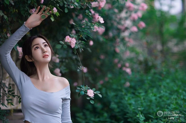 气质美丽女孩蔷薇花前驻足流连，着V领上衣搭牛仔裙艺术摄影图片