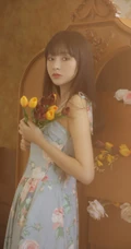 手拿郁金香的漂亮长发少女，身穿印花肩带裙在朦胧感的室内中举止动人