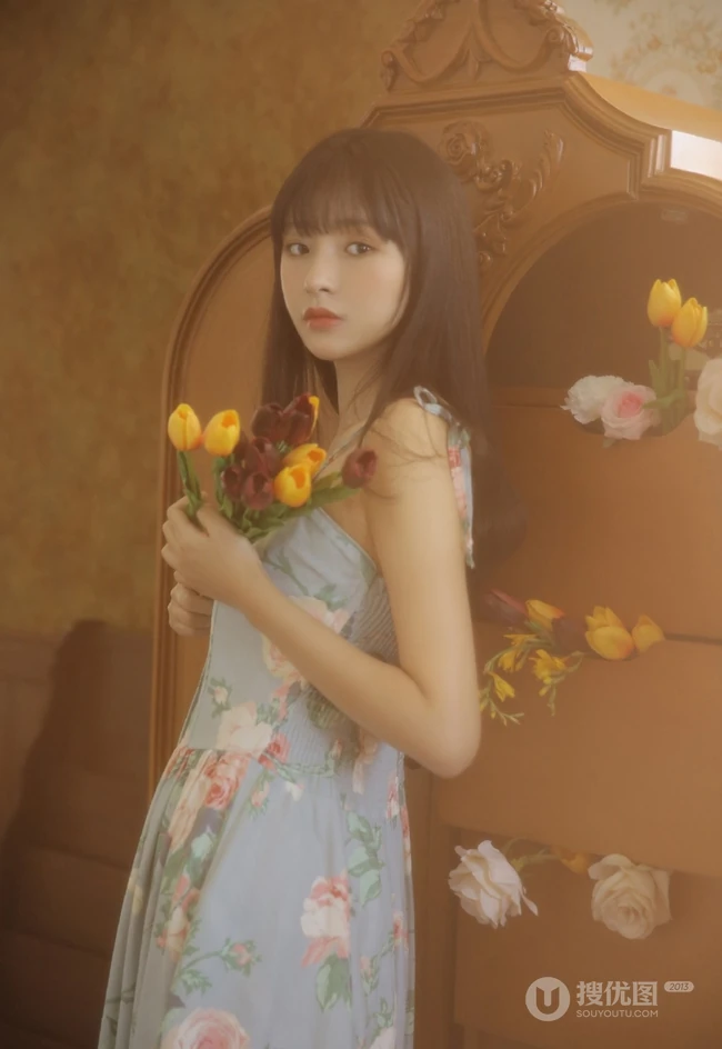 手拿郁金香的漂亮长发少女，身穿印花肩带裙在朦胧感的室内中举止动人