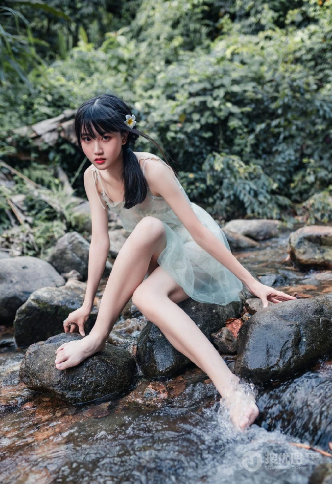 清澈见底的山间溪流中，一个穿着蓝色连衣裙的美丽麻花辫女孩摄影艺术照