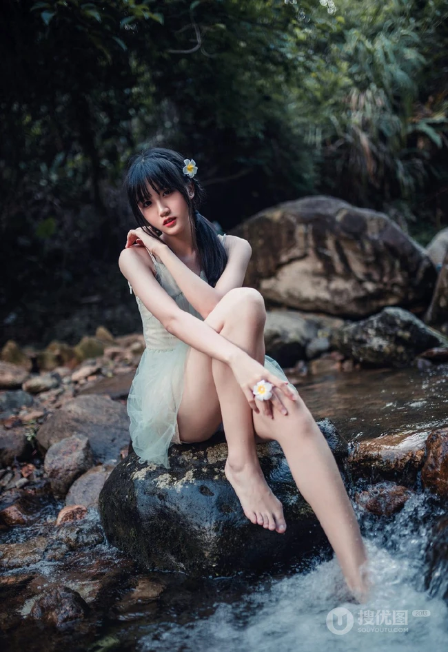 清澈见底的山间溪流中，一个穿着蓝色连衣裙的美丽麻花辫女孩摄影艺术照