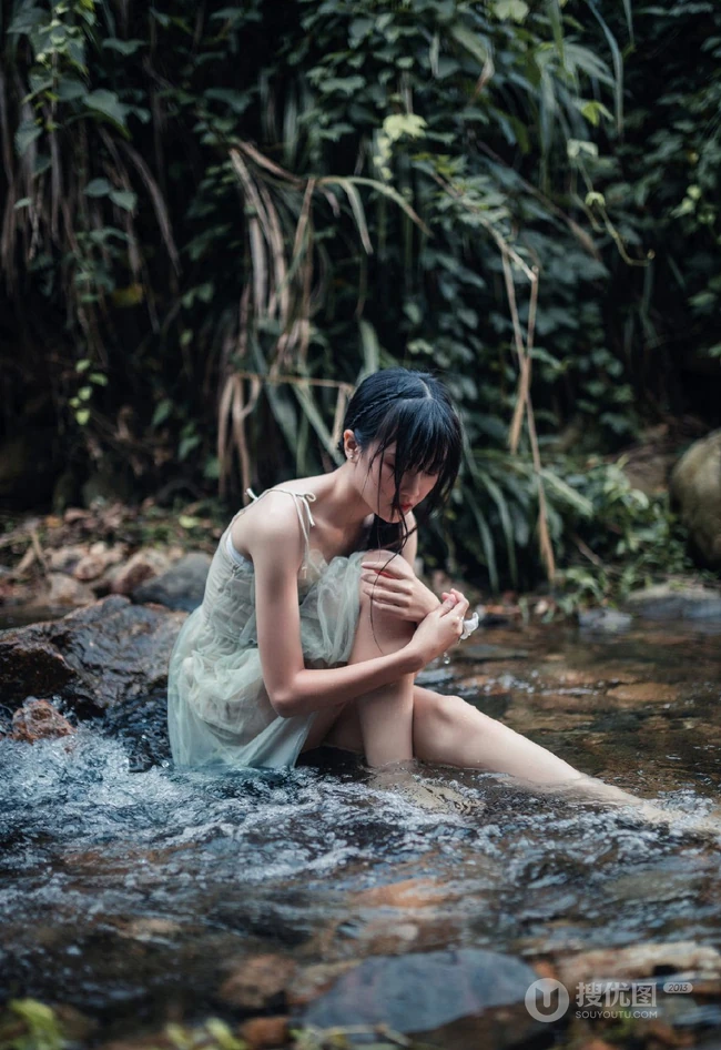 清澈见底的山间溪流中，一个穿着蓝色连衣裙的美丽麻花辫女孩摄影艺术照