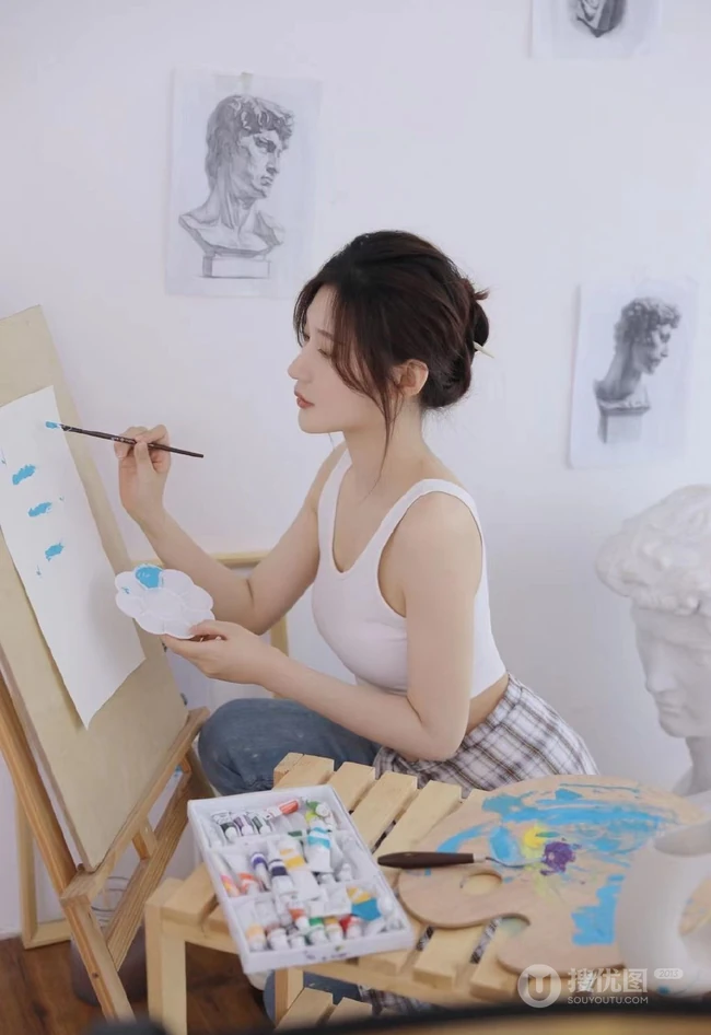 认真画画的样子好美，画室里穿着白色肩带文胸衣牛仔裤的女生写真图片