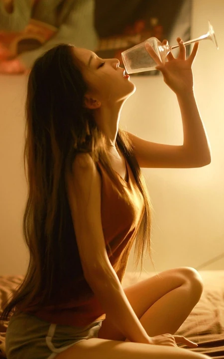 手拿高脚杯，盘膝坐在床上的背心短裤美女高清唯美手机壁纸图片