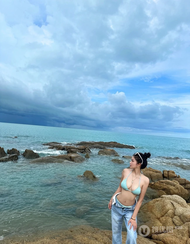 浪漫海边礁石上，身着蓝色肩带泳装加牛仔裤的优雅身形女生写真照片