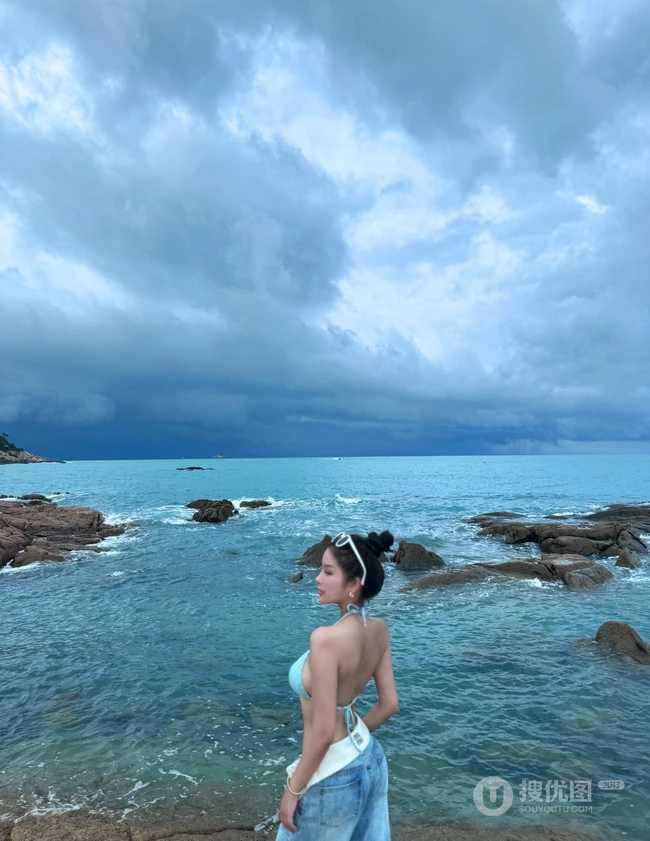 浪漫海边礁石上，身着蓝色肩带泳装加牛仔裤的优雅身形女生写真照片