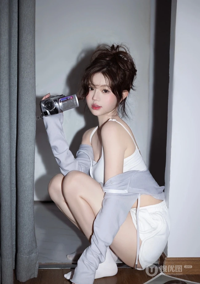娇俏动人，表情可爱的白色肩带礼裙衣短裤少女手拿相机居家写真照