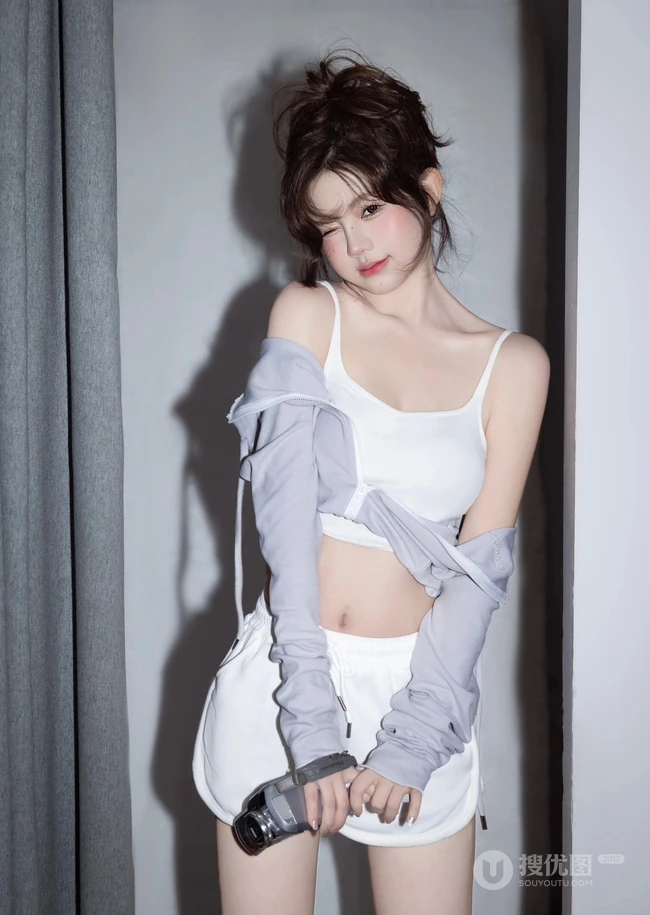 娇俏动人，表情可爱的白色肩带礼裙衣短裤少女手拿相机居家写真照