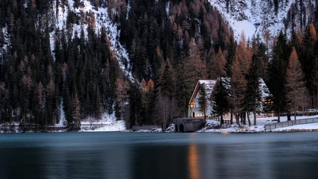 冬日湖边山林旁的亮灯小屋雪景
