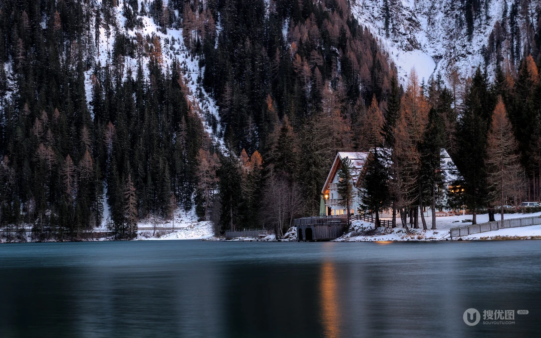 冬日湖边山林旁的亮灯小屋雪景